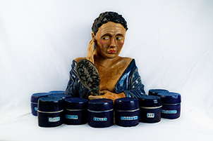 buste de femme en robe bleue avec des cheveux courts et sombres derrière un tas de bouteilles de crème