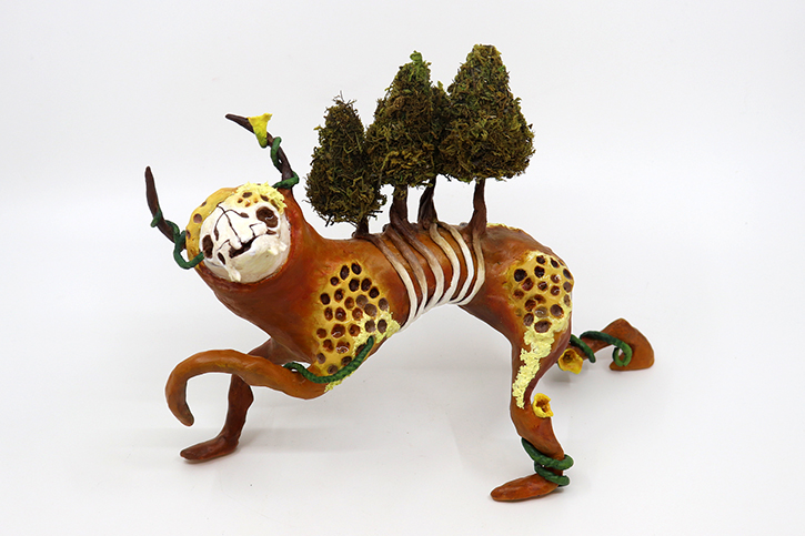 fantasy tiger-like sculpture with a human-like face and trees on its back against a white background